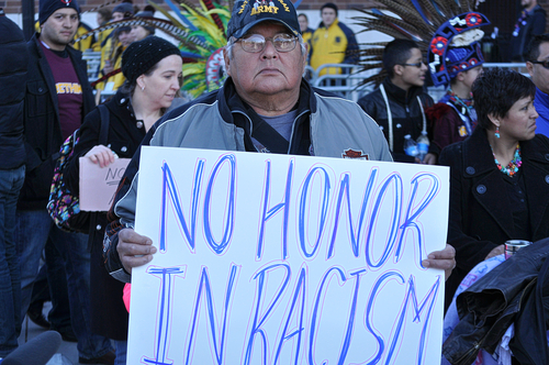 Picture shows a man holding a sign - No honor in Racism - demonstating for native amercian rights